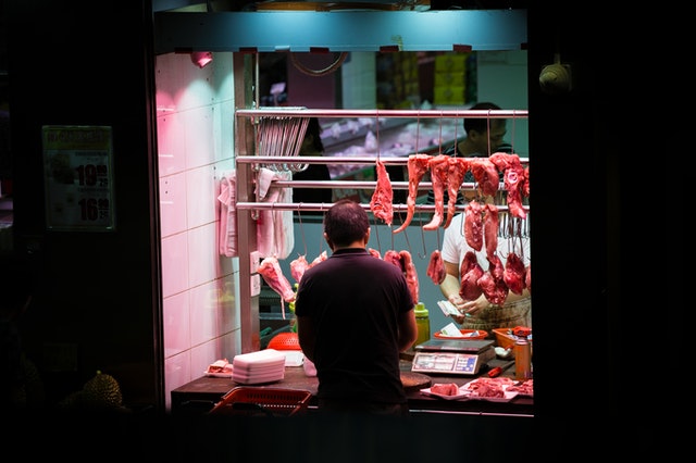 man-standing-in-front-of-stall-with-hanged-meats-2167025